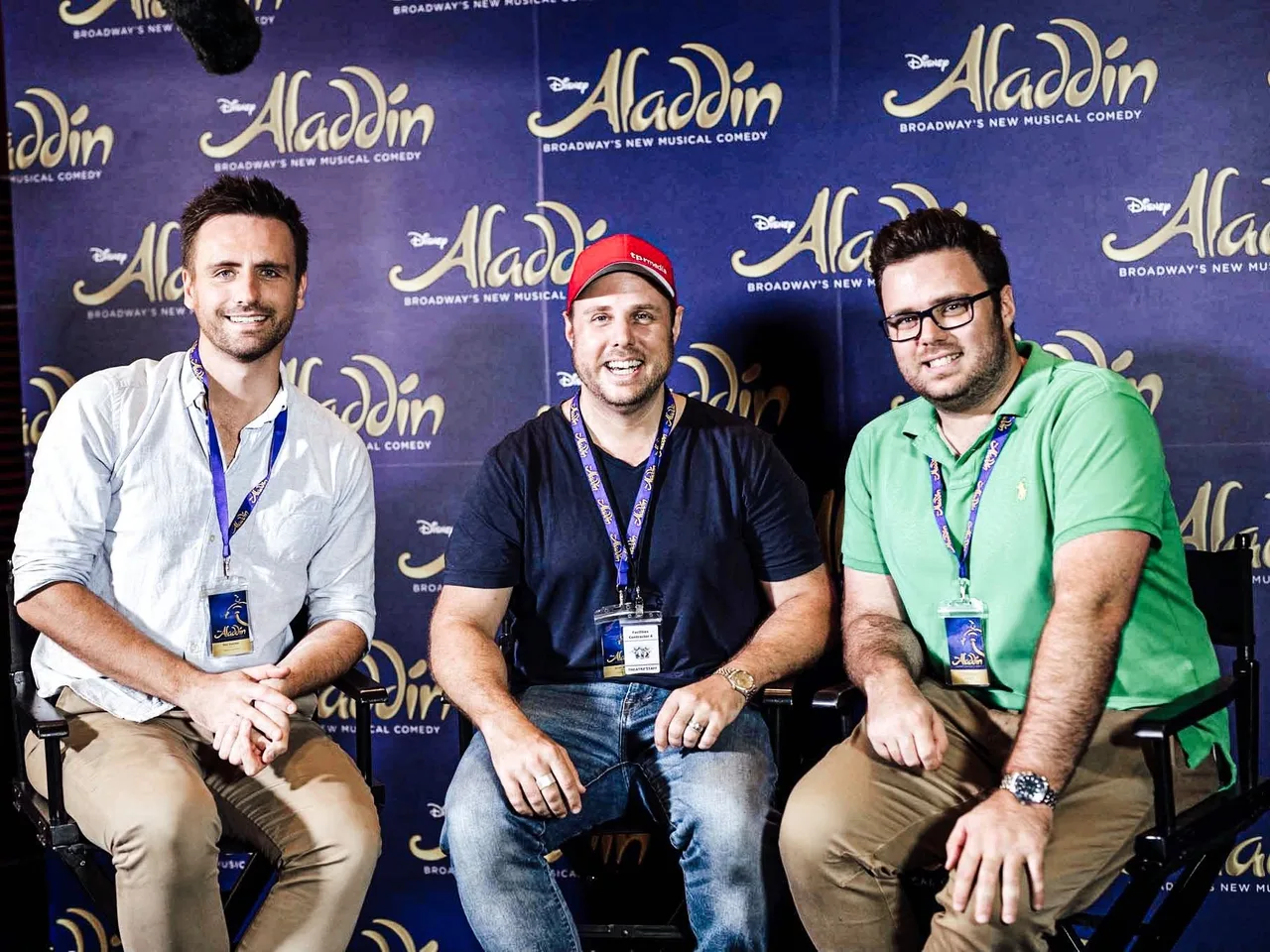 Three people seated in front of Disney's Aladdin the Musical backdrop during the Australian tour