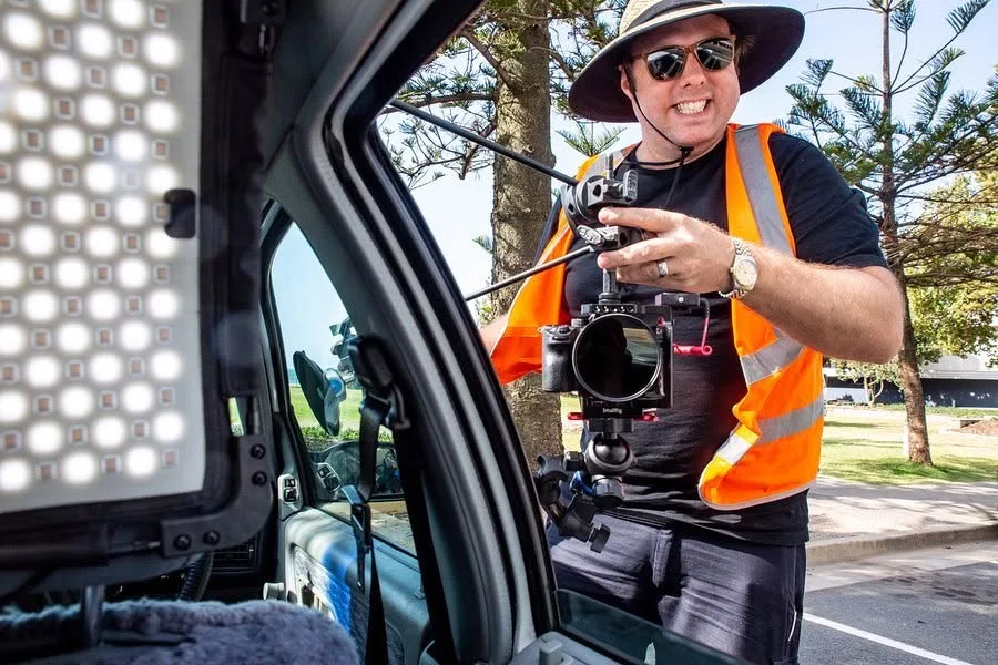 A camera operator with cinema camera and lighting beside the car during the Coolangatta shoot