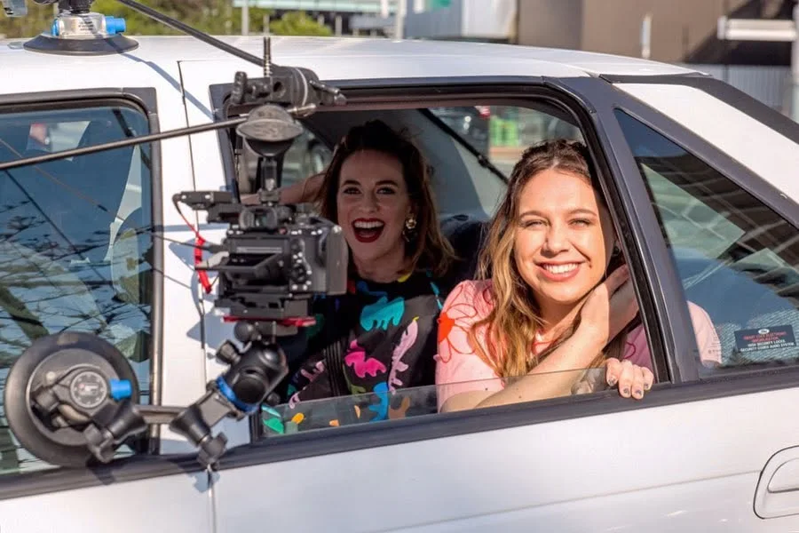 Natalie Abbott and Stefanie Jones in the car with a mounted camera filming the Muriel's Wedding promotional scene