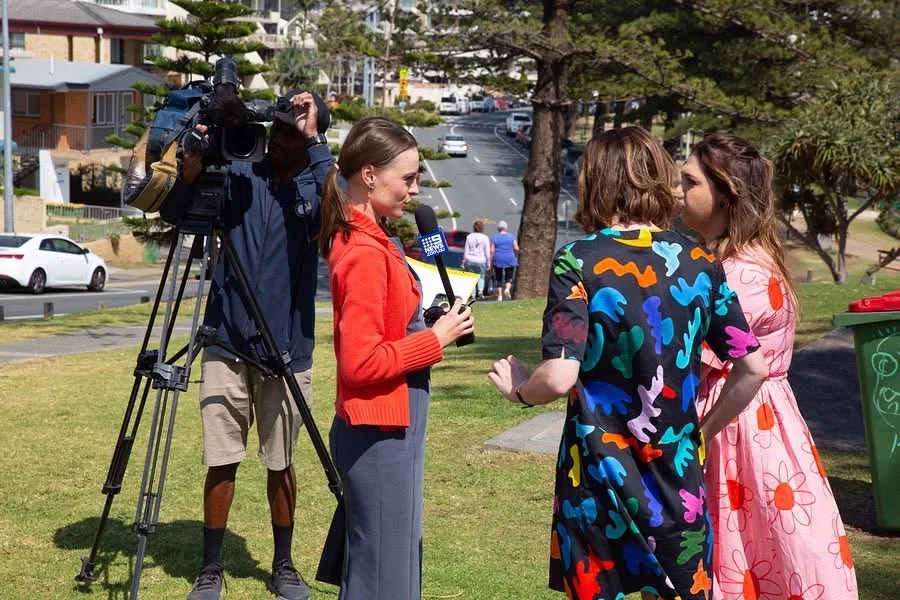 A television camera crew and reporter interviewing the musical's stars during the Coolangatta shoot