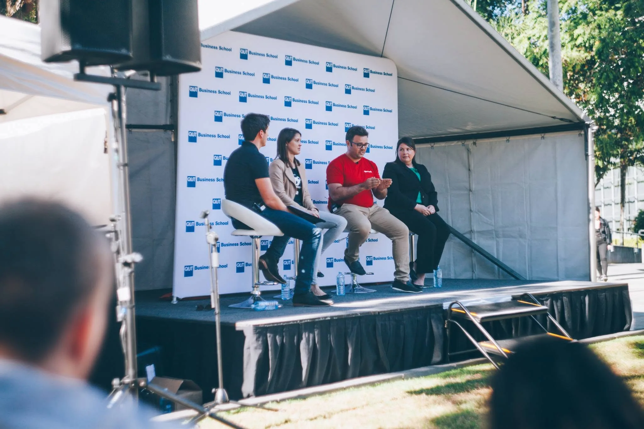 Tim Nelson participating in a panel discussion on stage with a QUT Business School backdrop at Gardens Point